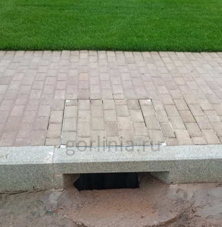 Установленный на дорожке уличный люк Драго, вымощенный брусчаткой в раскладку покрытия Установленный на дорожке уличный люк Драго, вымощенный брусчаткой в раскладку покрытия